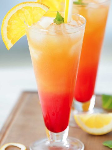 red and orange {title:2:5} mezcal sunrise in a glass with lemon wedges
