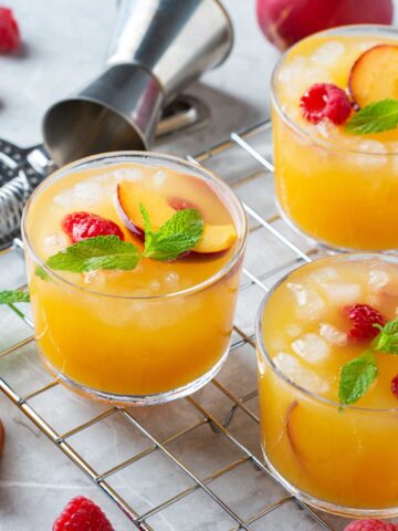 three peach {title:2:3} on a countertop with a small shaker, topped with raspberries and other garnishes